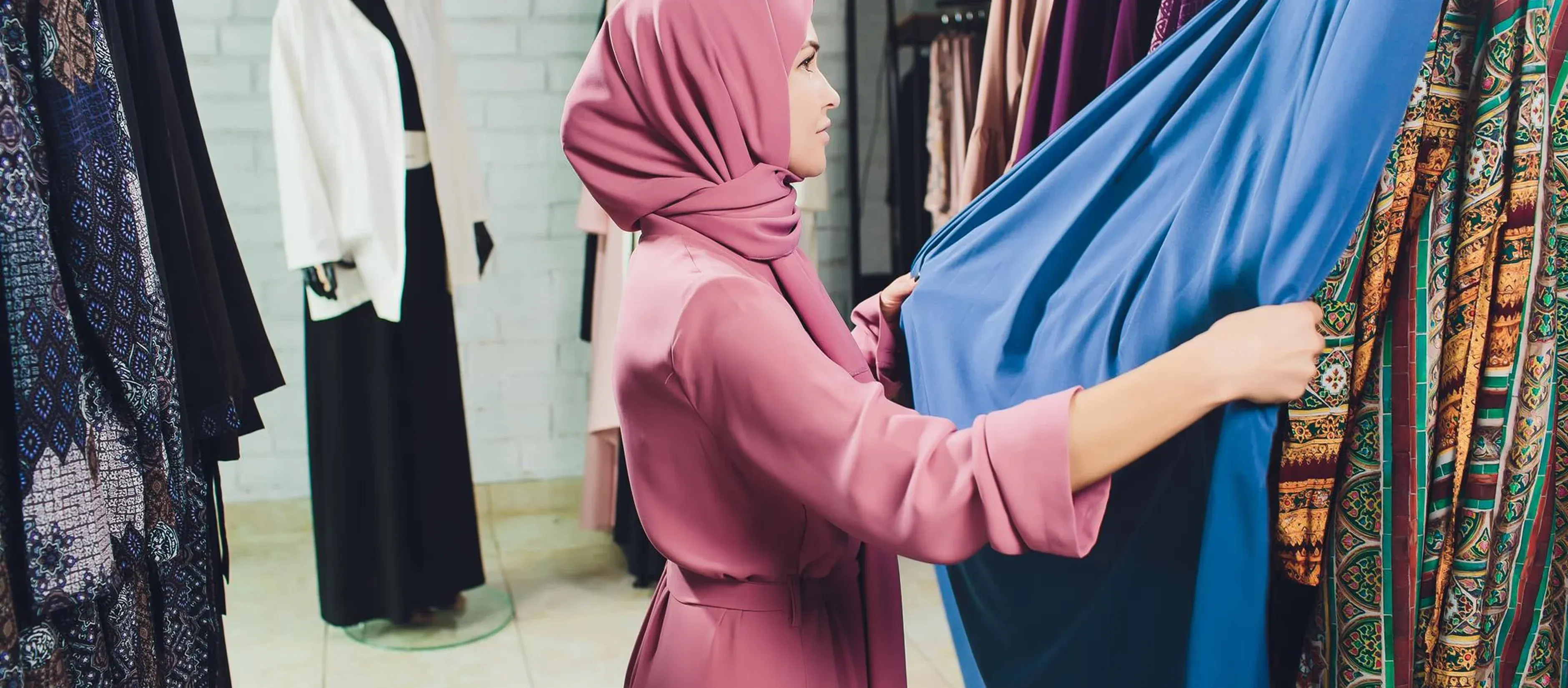 A woman in a pink hijab browsing racks of abayas and dresses at the display center
